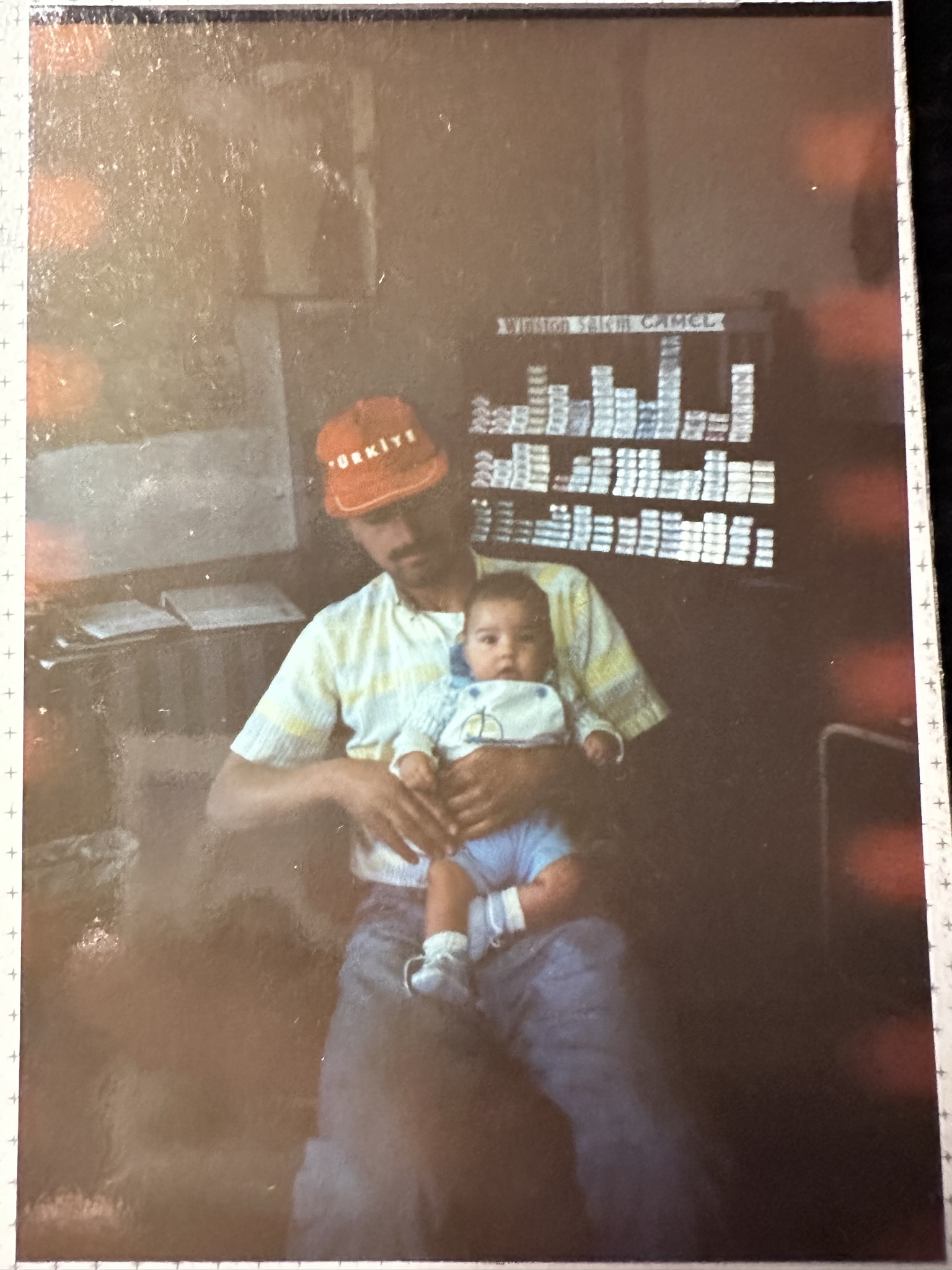 A baby held by his father in front of tobacco shelves — the beginning of a family legacy in the tobacco business.